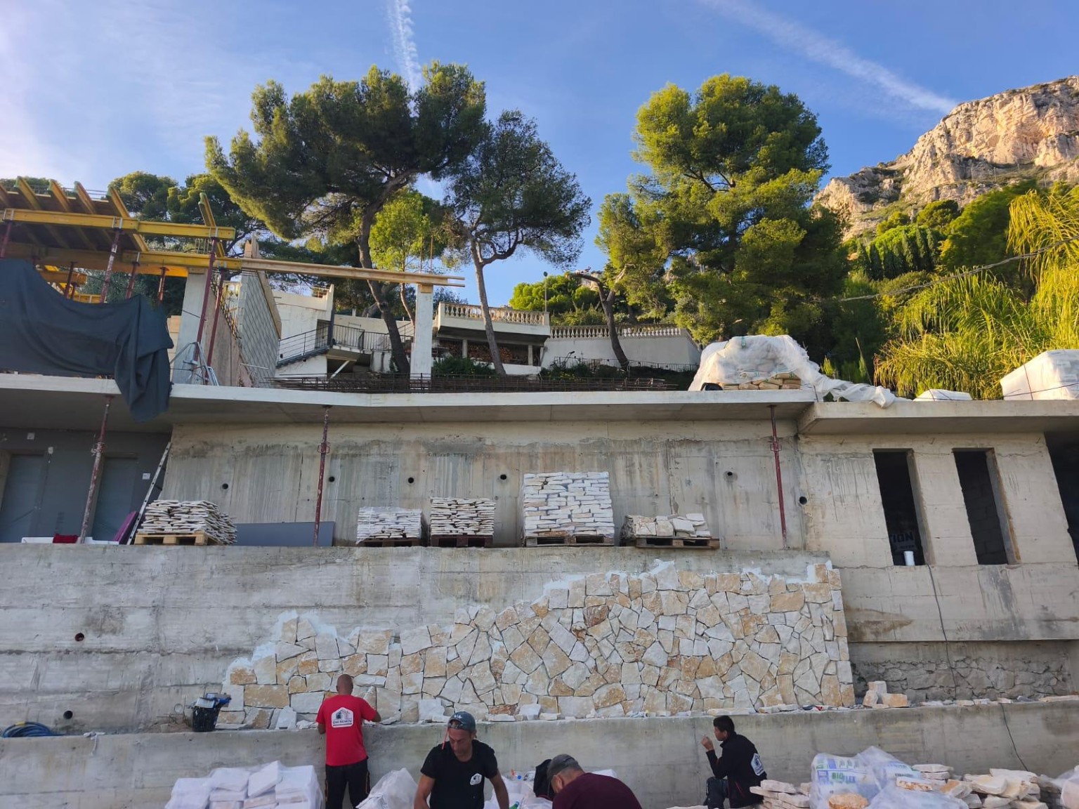 Mur en pierre naturelle à pièces irrégulières en cours de pose, avec palettes sur le chantier